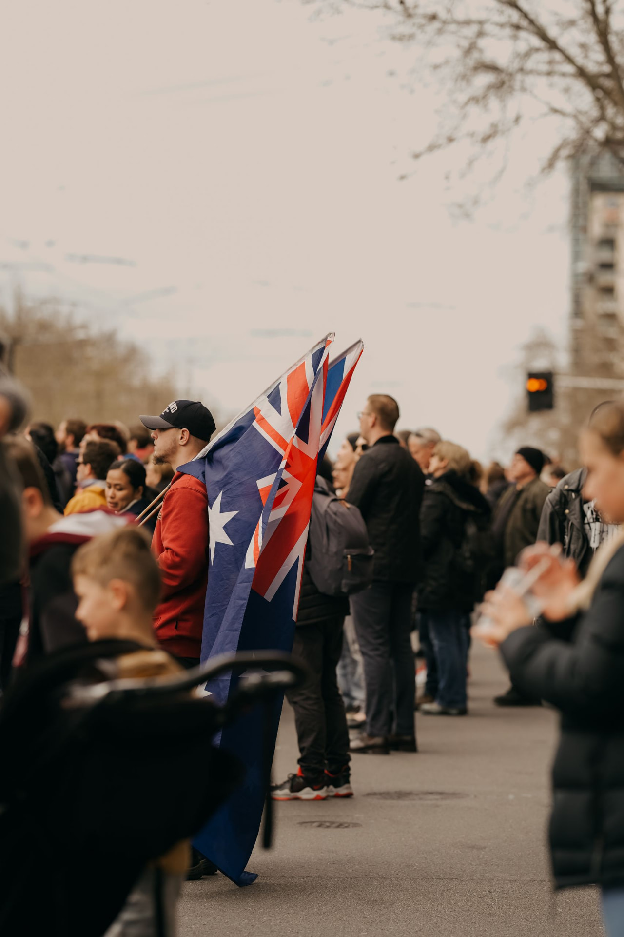 A man wearing an Australian flag standing in a crowd lining a street