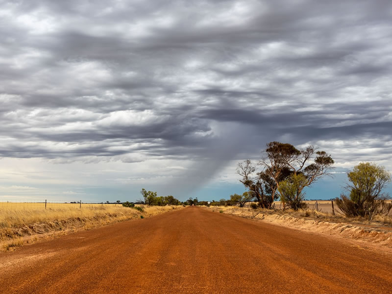Straight red dirt road under heavy grey storm clouds