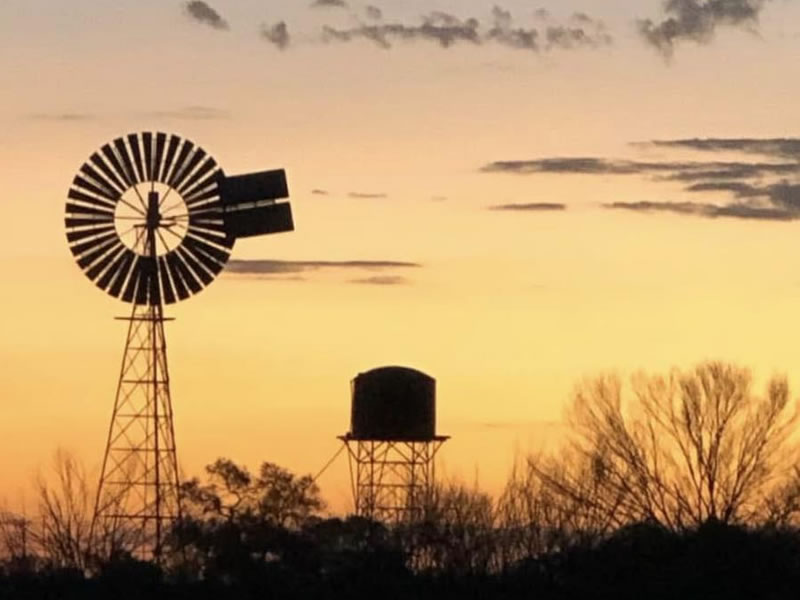 Silhouette of a windmill and water tank against a golden dusk sky