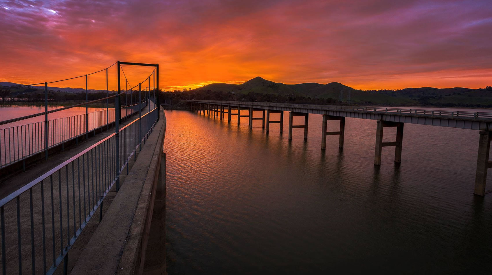 Bridge across a lake at sunset with hills silhouetted behind