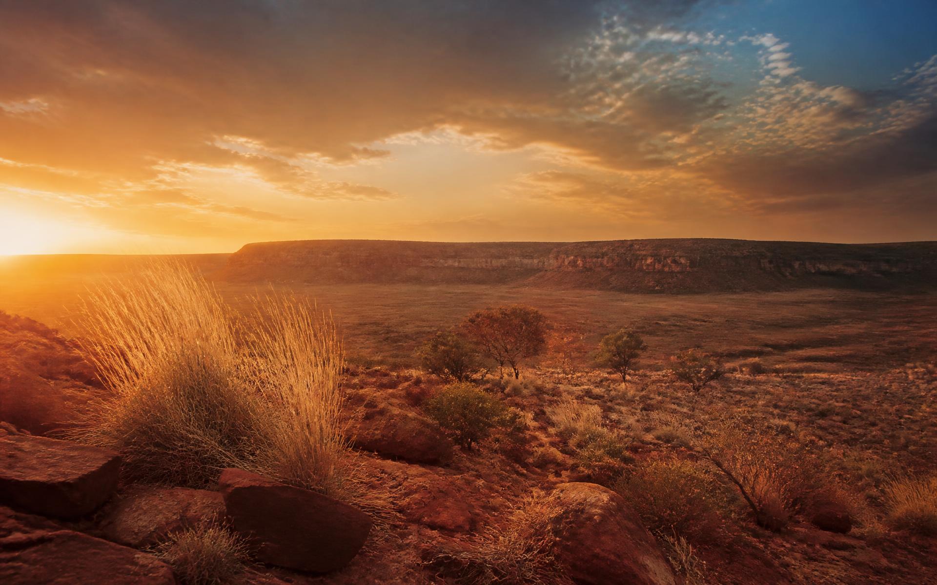 The Australian red centre at golden hour, ochre earth beneath a vast sky